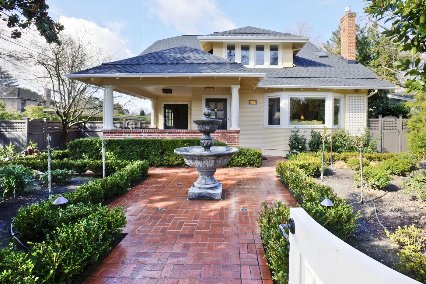 Brick path to the front porch past clipped box hedging and a stone fountain