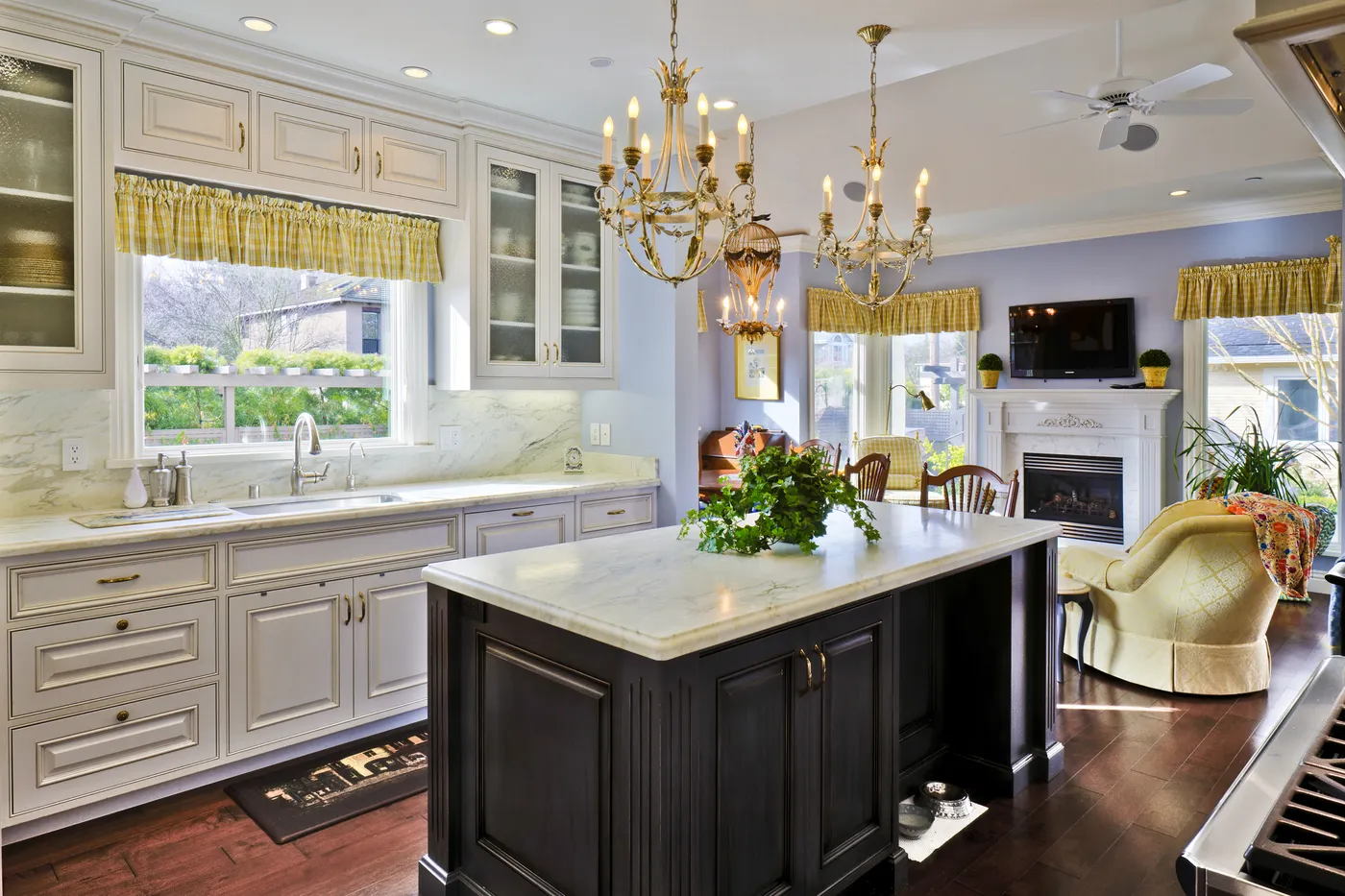 Kitchen with a dark island below paired chandeliers, open to the family room