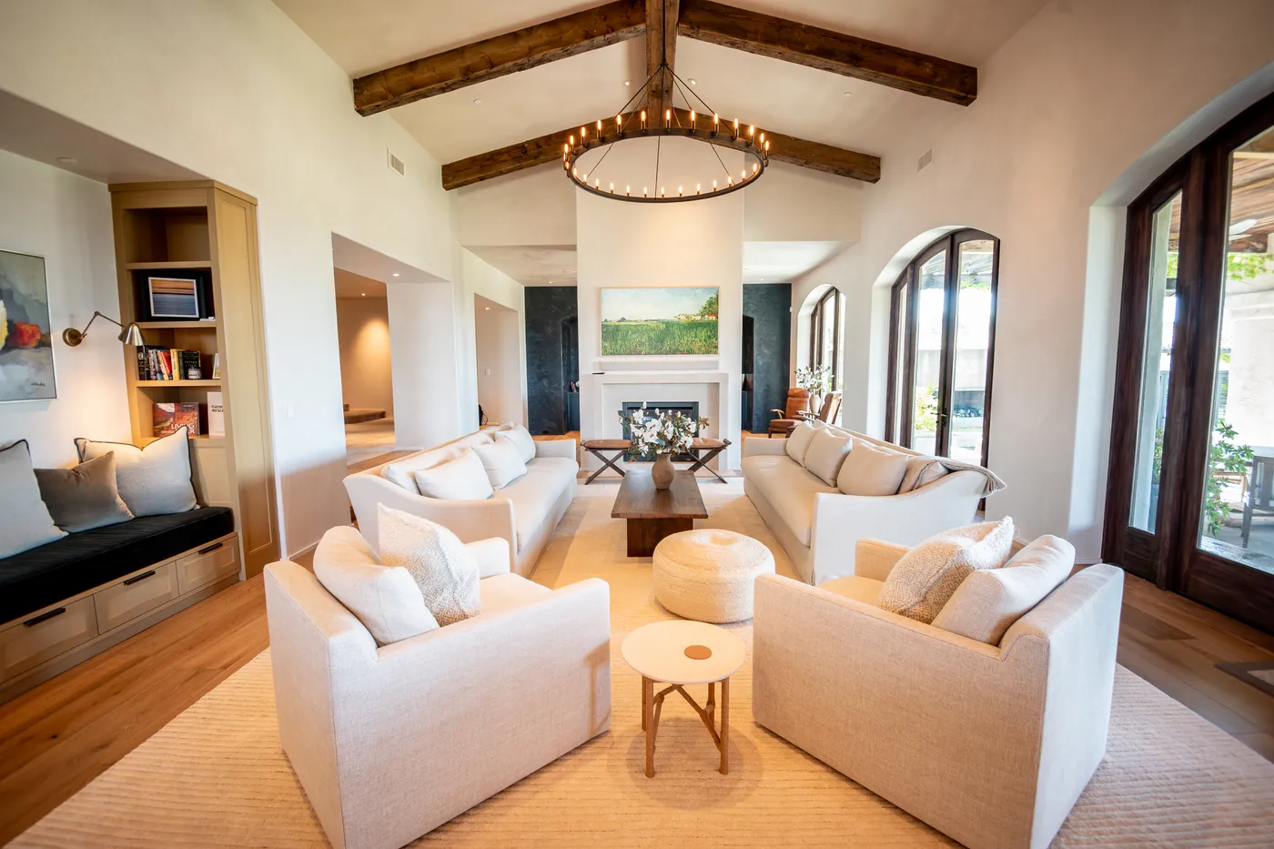 Living room under a vaulted beamed ceiling with a ring chandelier and a built-in window seat