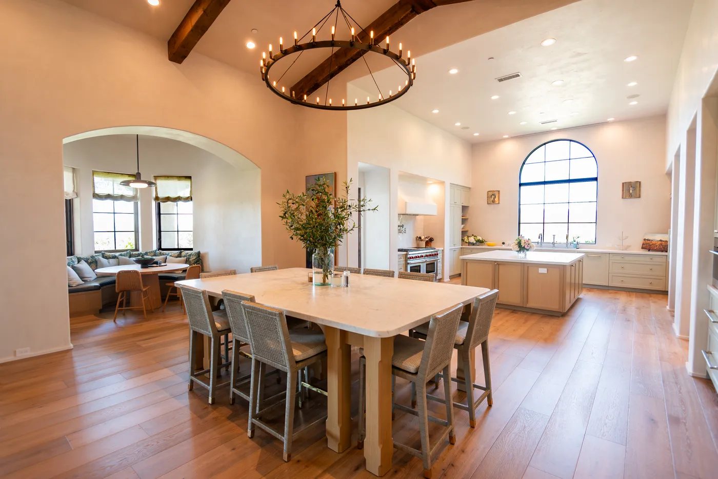 The opened kitchen with a long central worktable below a ring chandelier and exposed beams