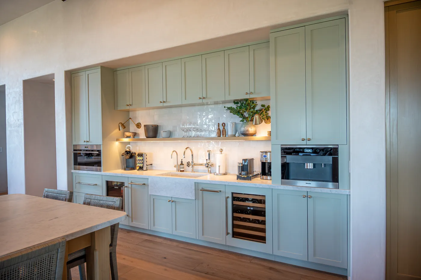 Perimeter cabinetry with a farmhouse sink, built-in coffee machine, wall oven and wine storage