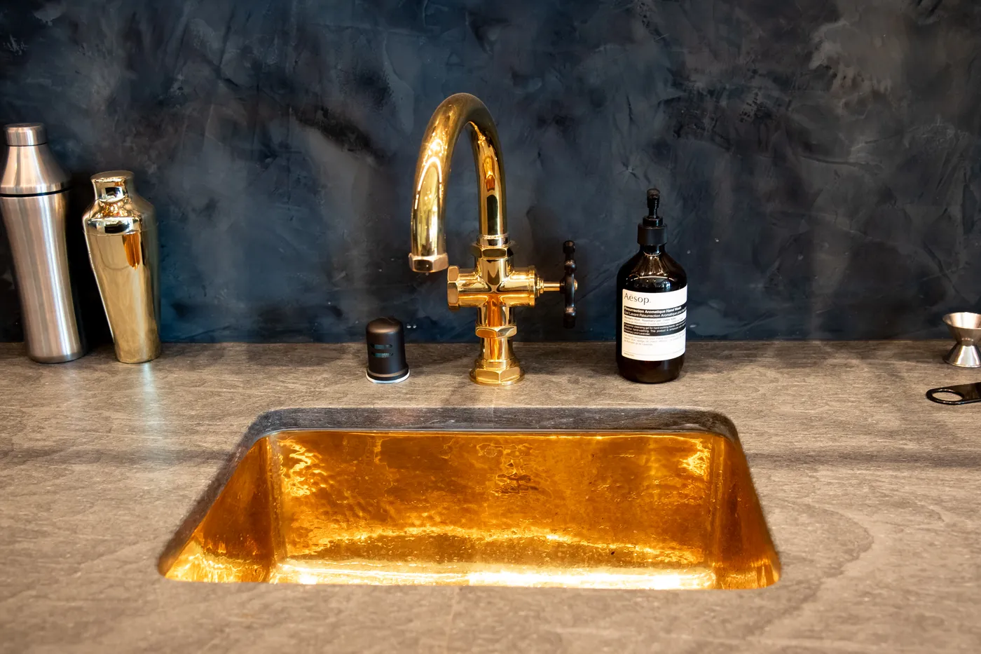 Hammered brass bar sink and faucet against the dark plaster backsplash