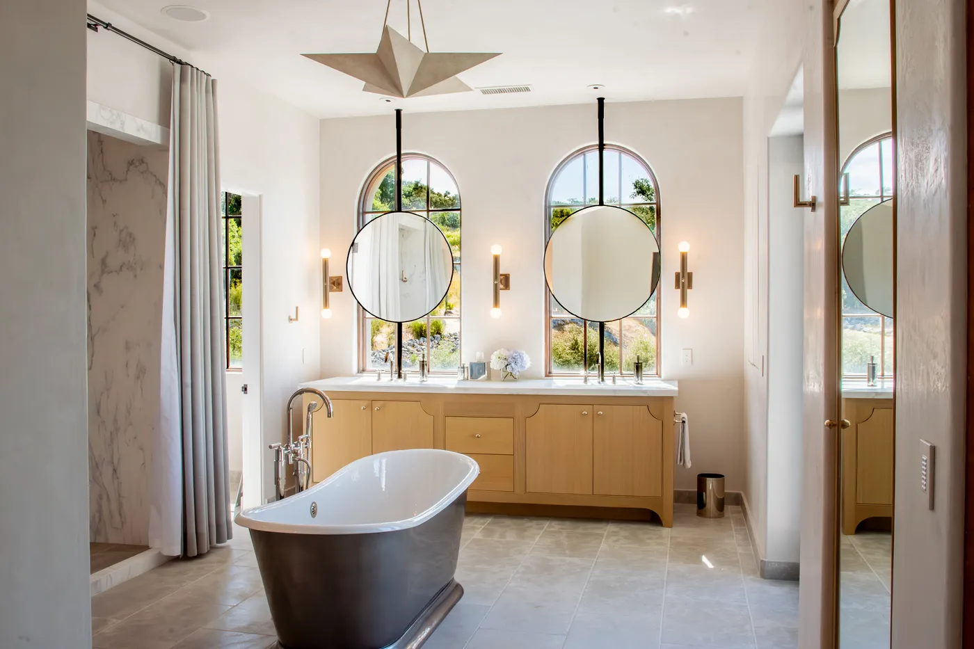 Primary bath with a freestanding tub, oak double vanity and round mirrors on arched windows