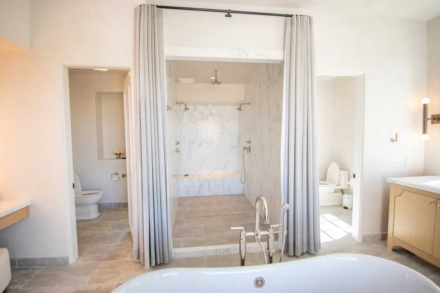 Marble walk-in shower between the two water closets, seen past the tub