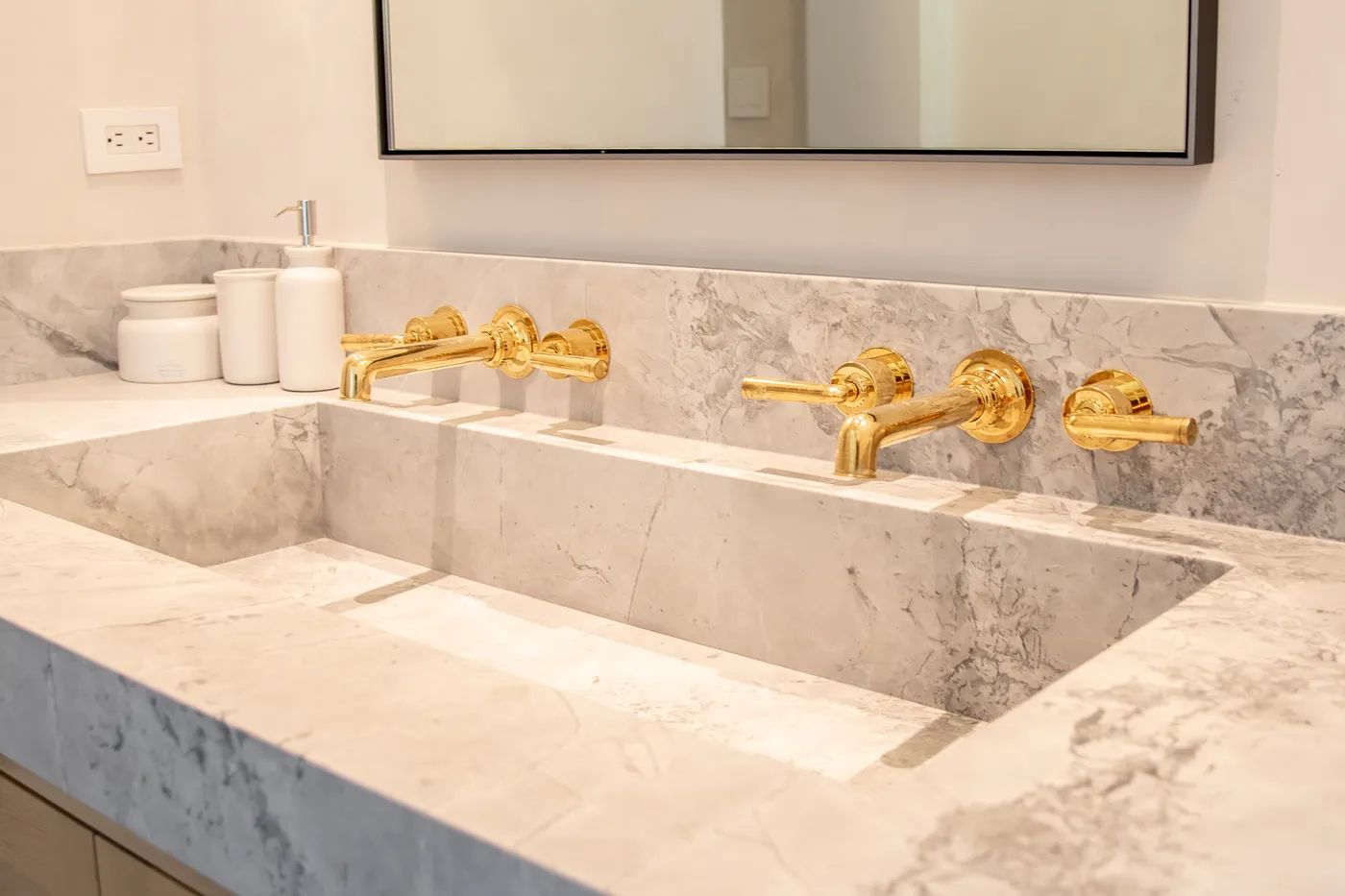 Marble trough sink with three wall-mounted brass faucets