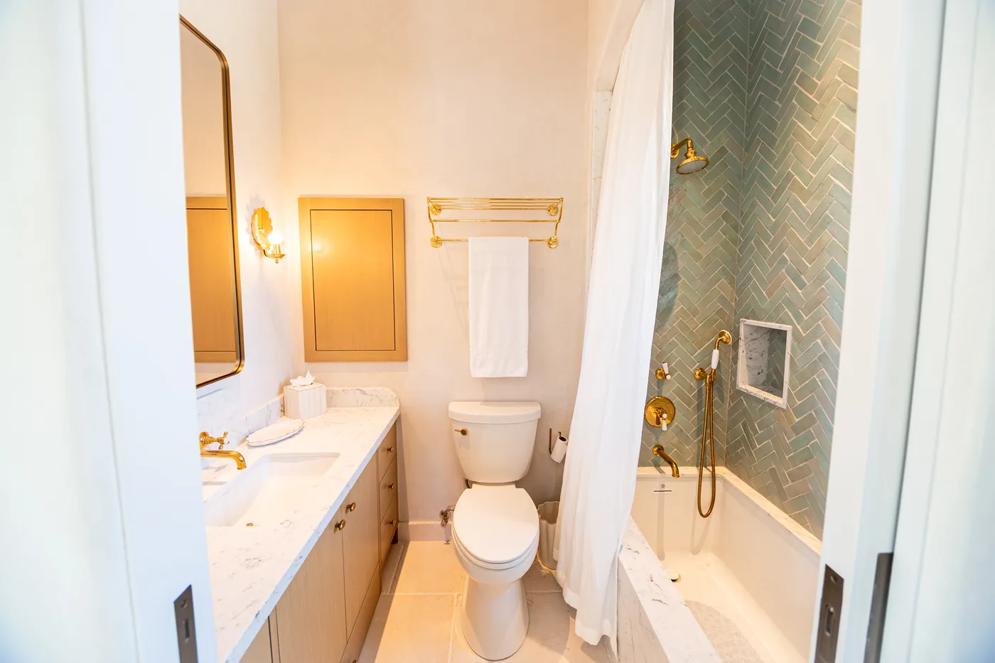 Guest bath with a green herringbone-tiled tub and shower and a marble vanity