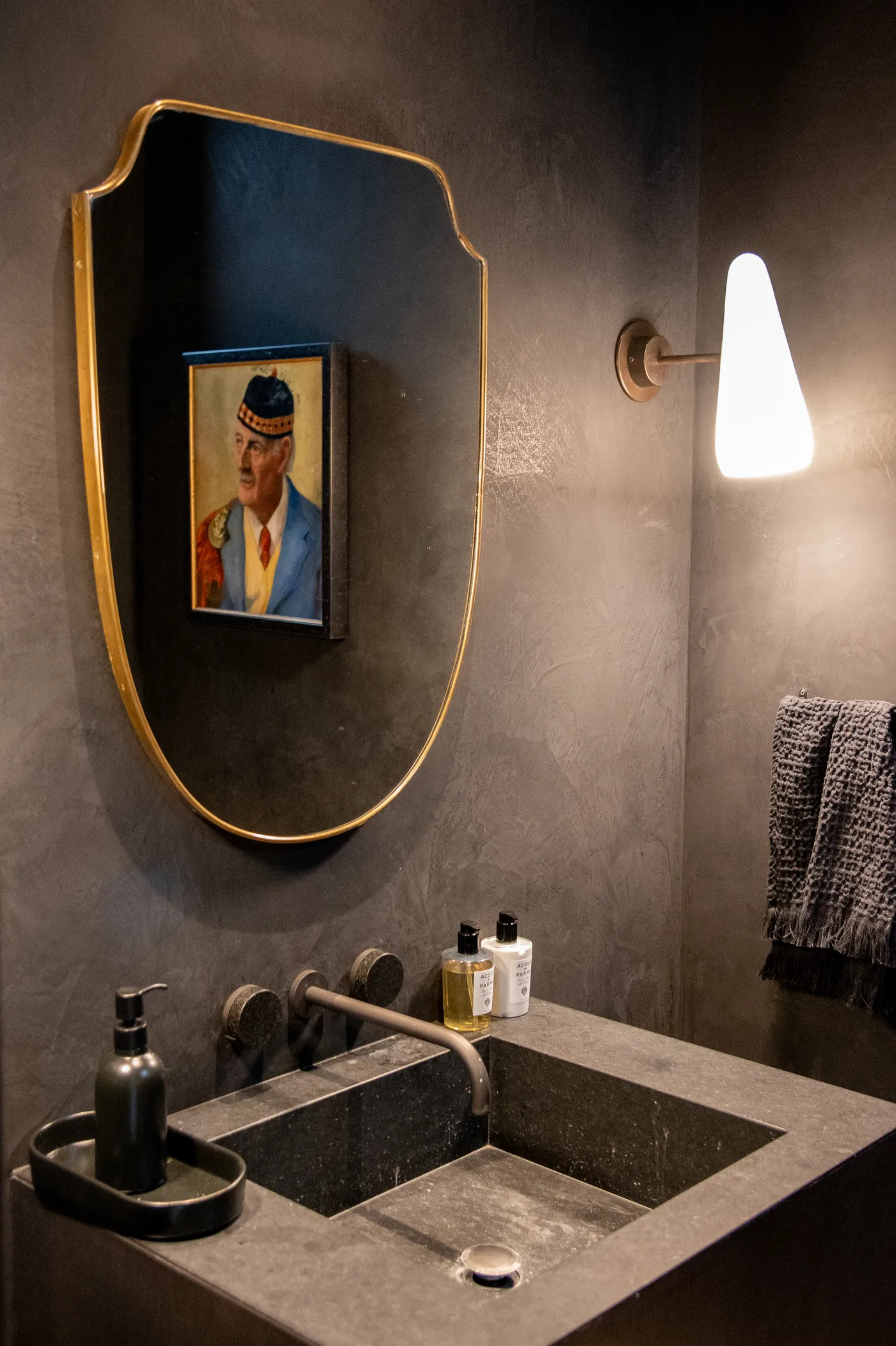 Powder room with dark plaster walls, a brass mirror and a stone sink