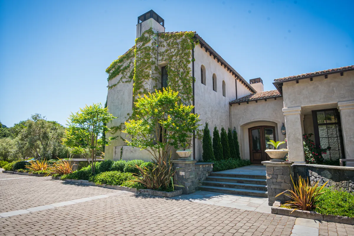 The stucco house and its clay tile roof above the paver motor court, ivy climbing the tower