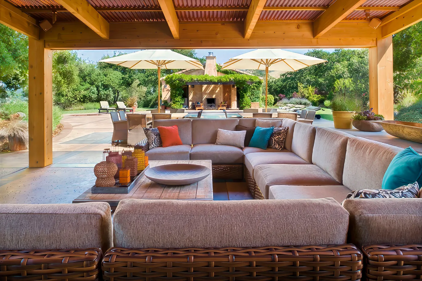 Wicker sectional under the timber roof, looking out to the pool and its umbrellas