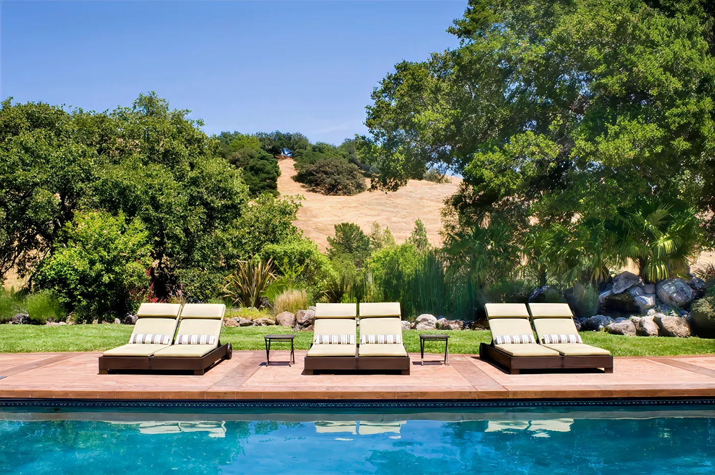 Three pairs of loungers along the pool, the hillside rising behind