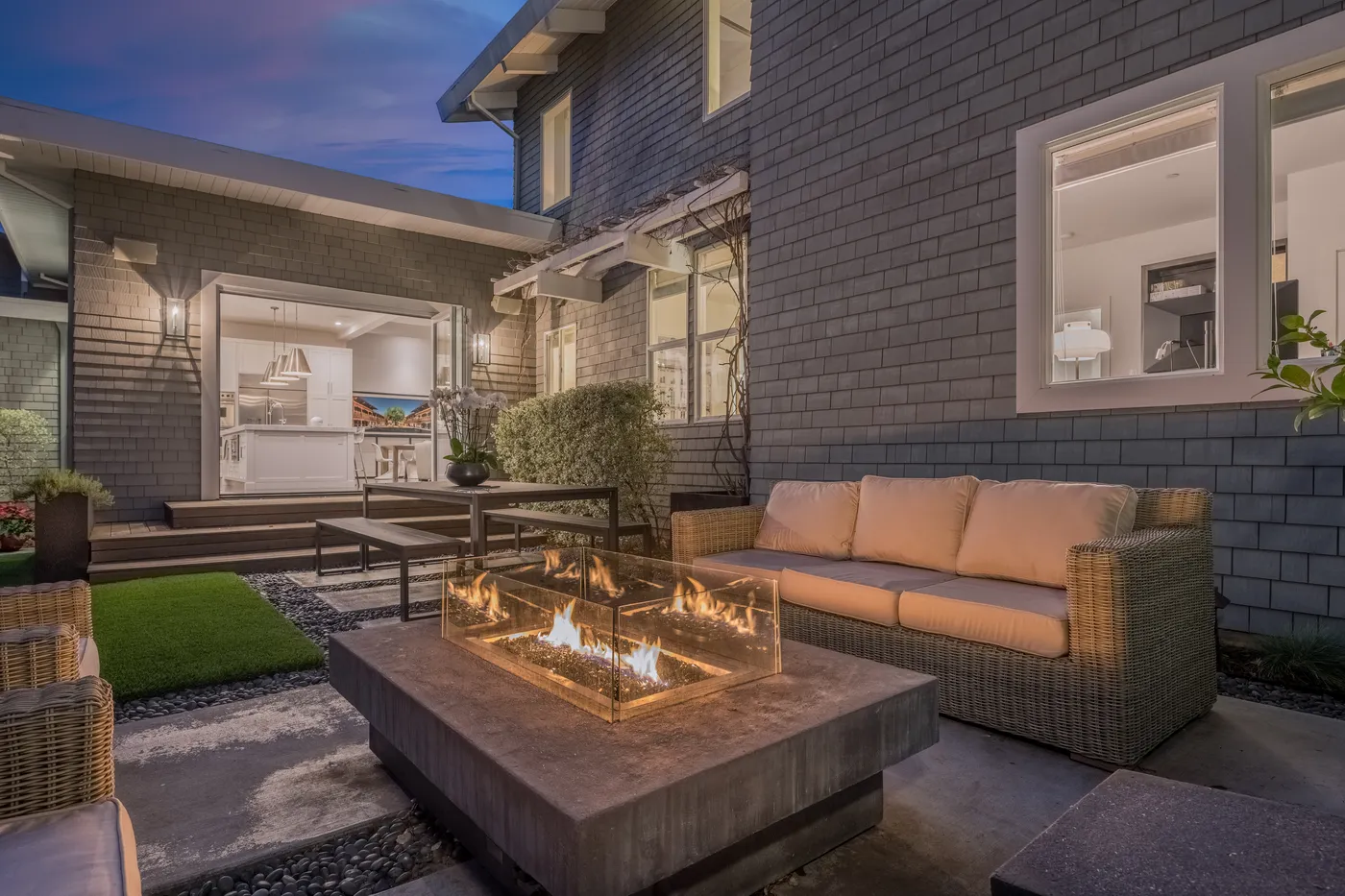 Outdoor sofas around a gas fire table at dusk, the house lit behind