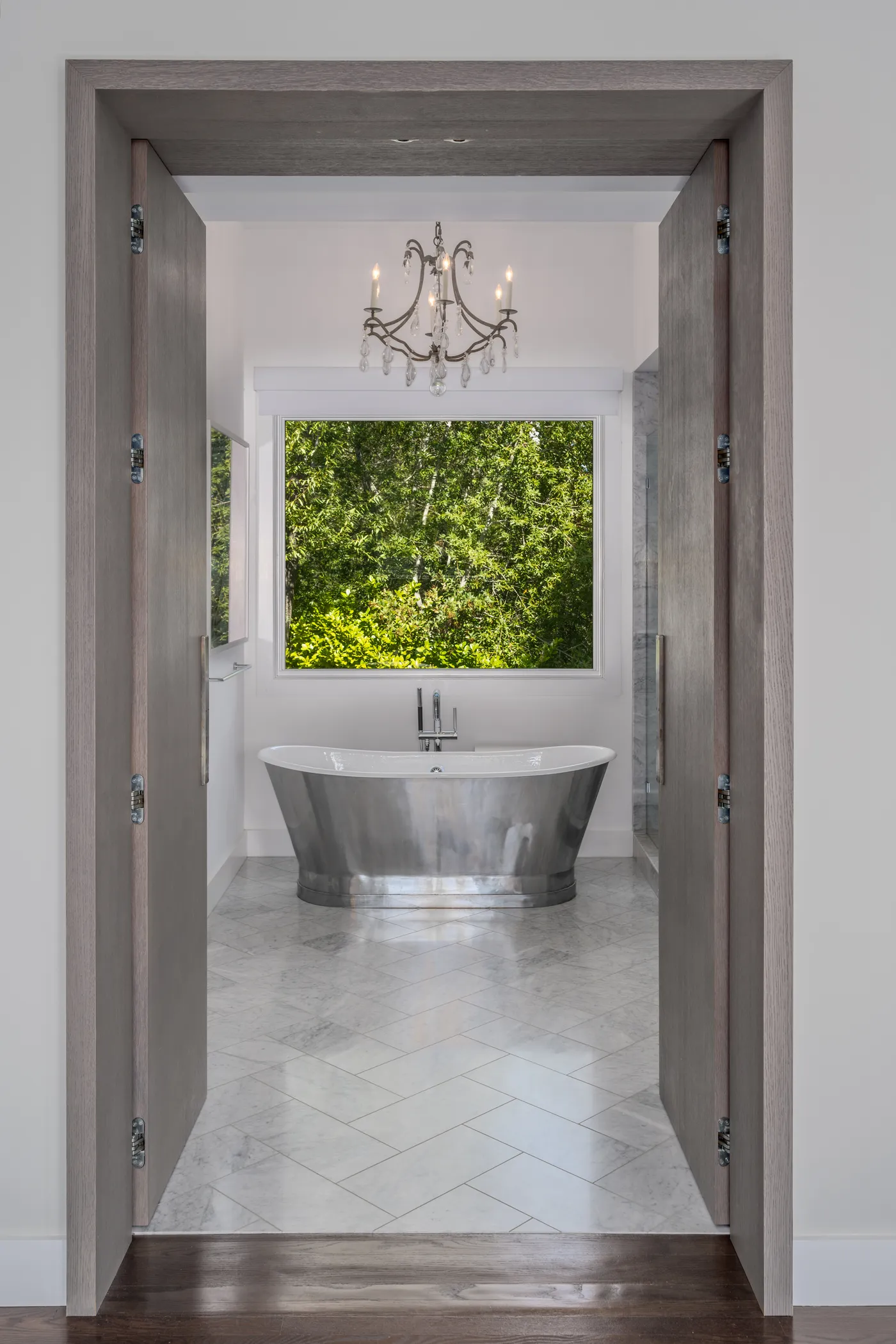 Freestanding metal tub in a marble alcove beneath a garden window