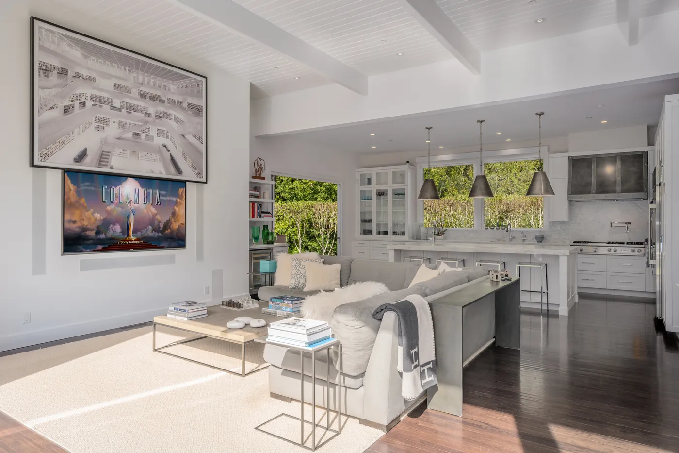 Living room under a vaulted white ceiling with the kitchen behind