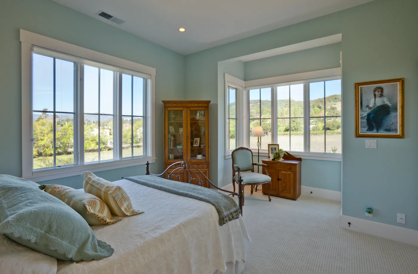 Bedroom in blue-green with windows on two sides looking to the hills