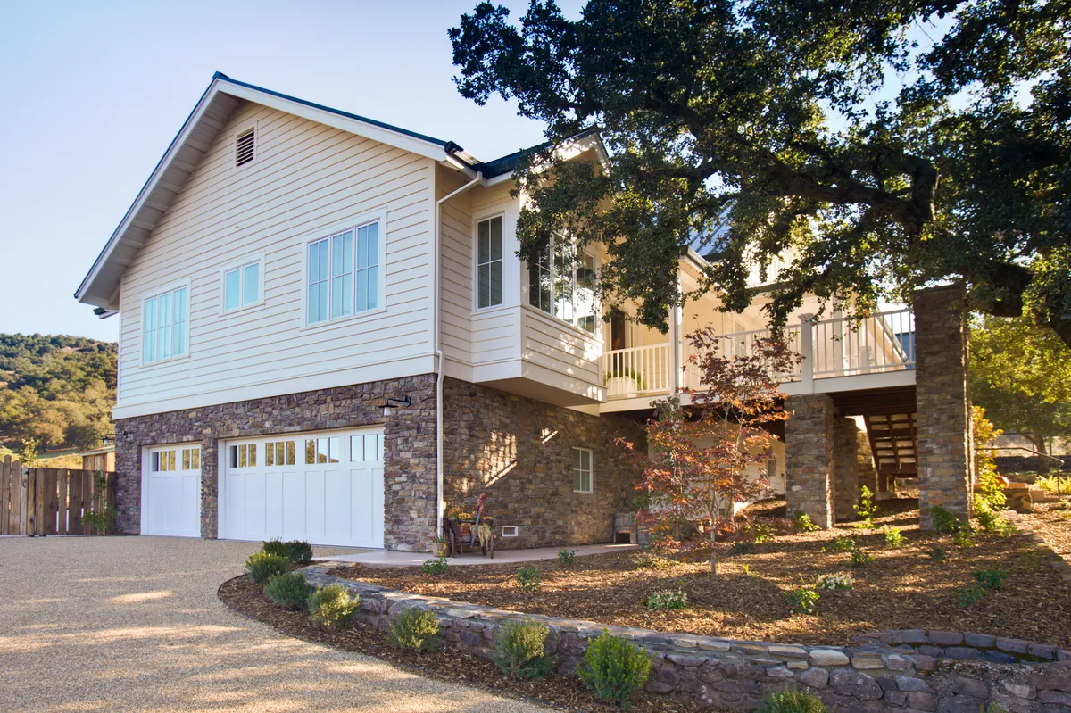 The new house from the front, white clapboard above a stone base with a covered porch and gabled dormer