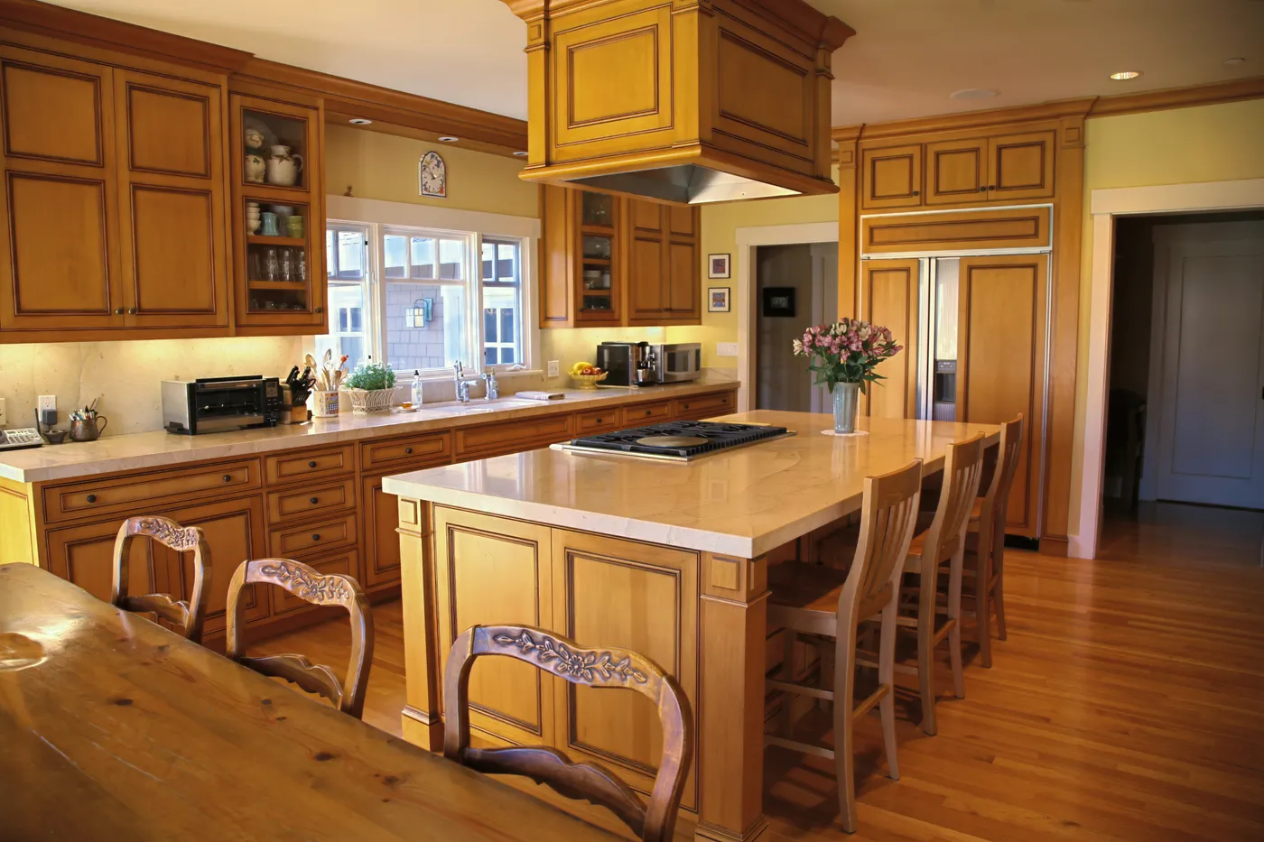 Kitchen island with a stone top, cooktop and seating under a boxed hood