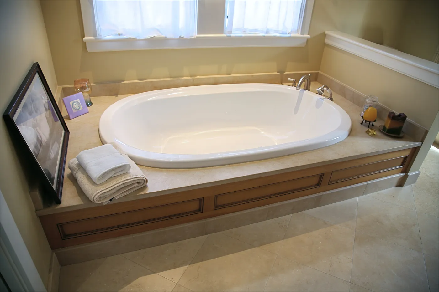 Oval soaking tub in a stone-topped surround below a shuttered window