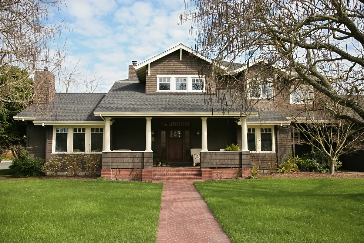 Shingled Craftsman house with a deep front porch at the end of a brick path