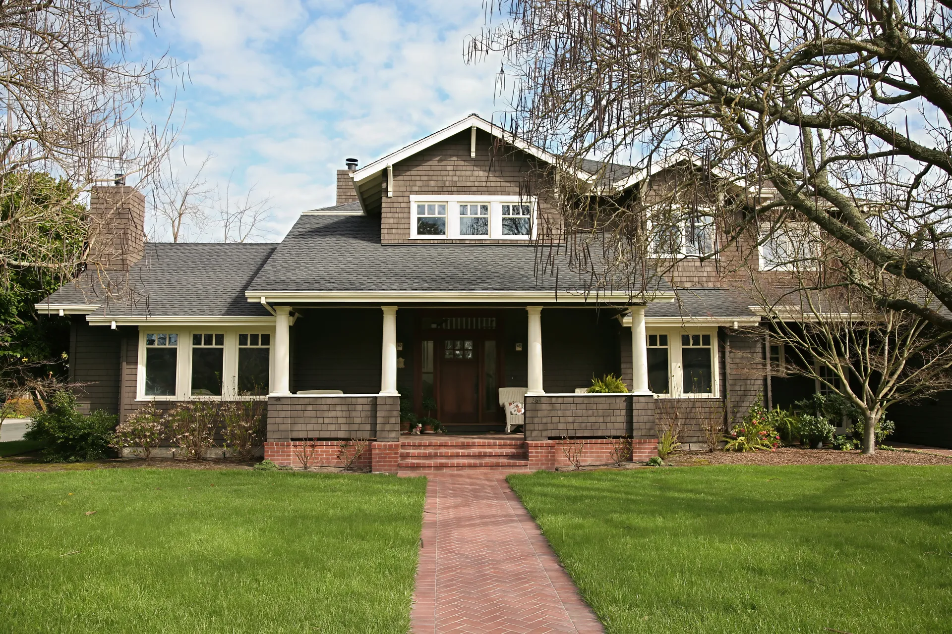 Shingled Craftsman house with a deep front porch at the end of a brick path