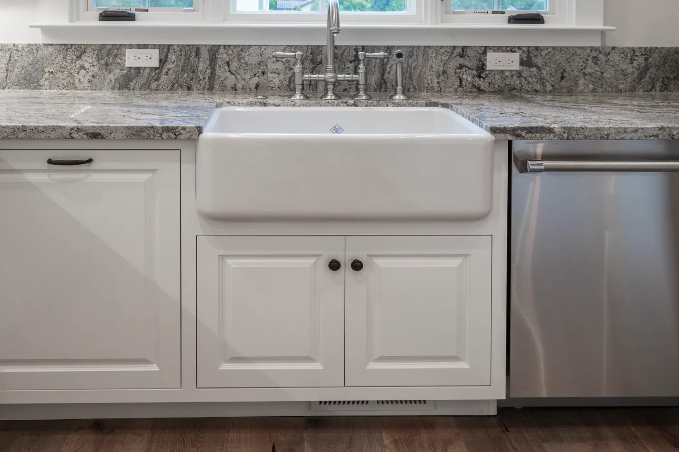 Farmhouse sink set into granite between panelled cabinet doors