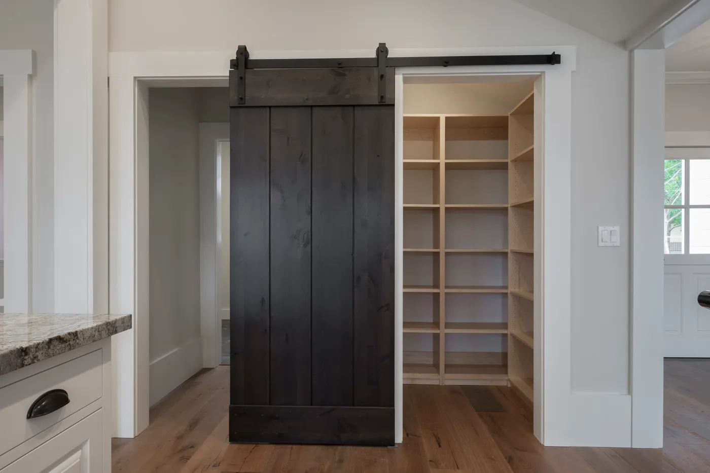 Dark barn door slid back from the pantry and its full-height shelving