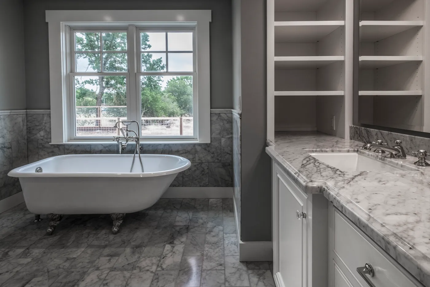 The primary bath from the vanity side, with built-in shelving beside the tub