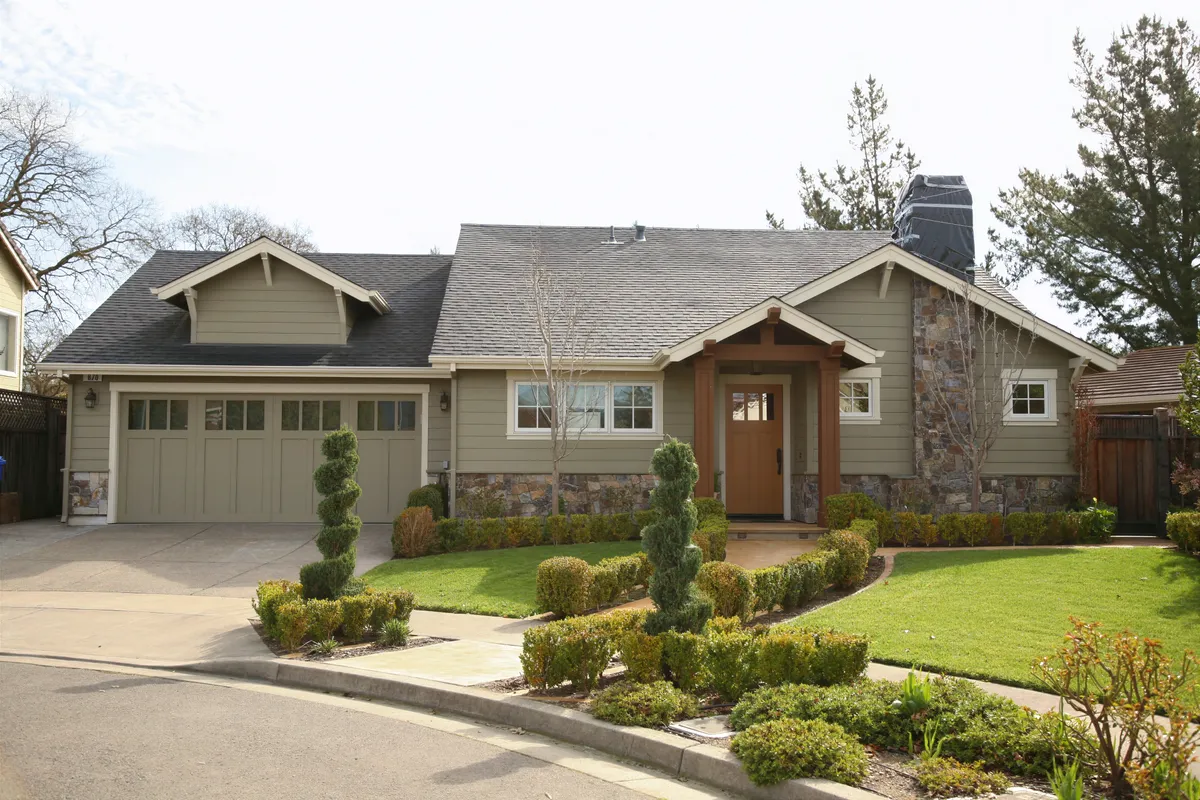 The Craftsman house from the street, olive siding above a river stone base with a timber porch