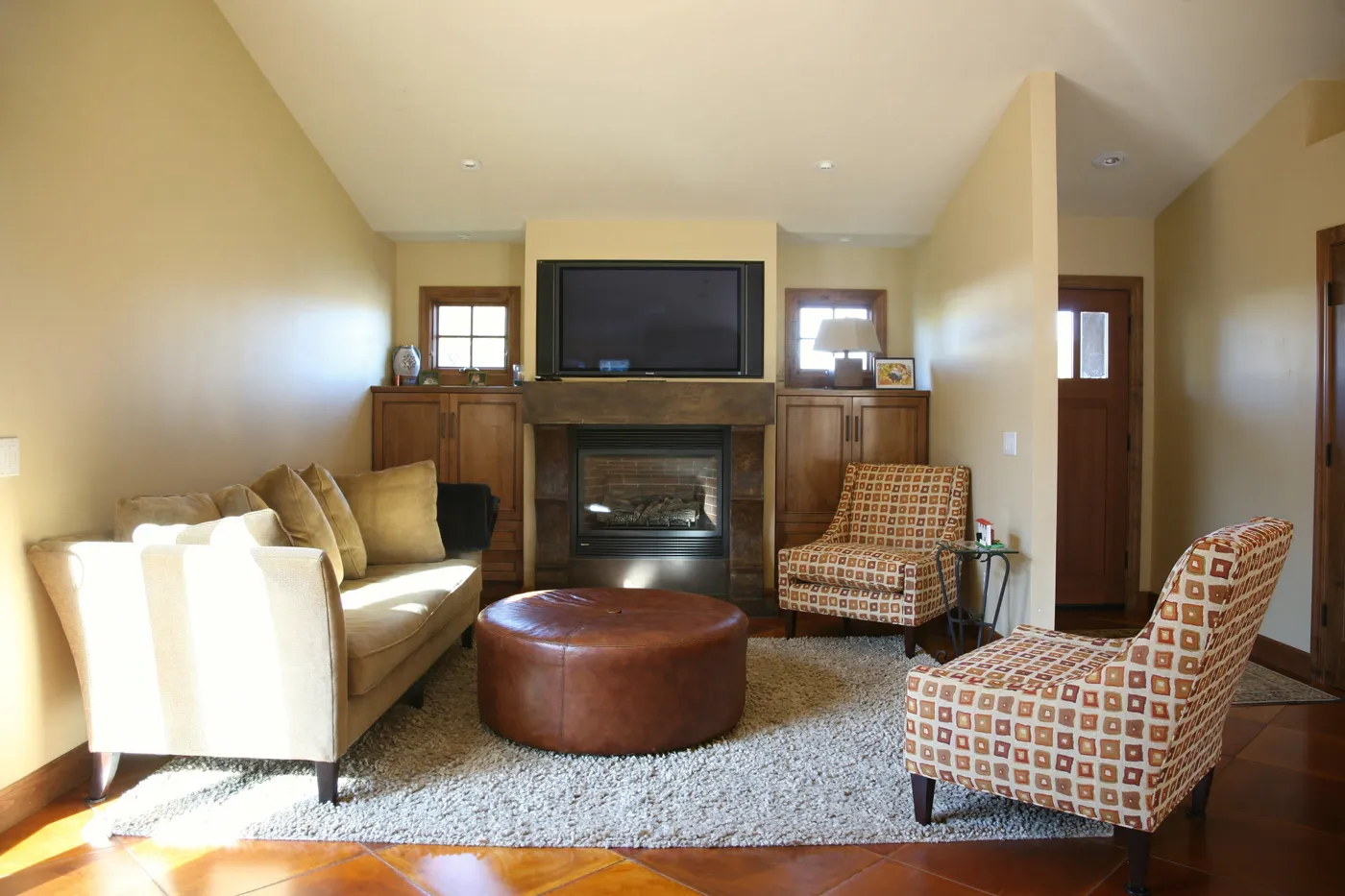 Living room with a fireplace below a wall-mounted screen, flanked by cabinets