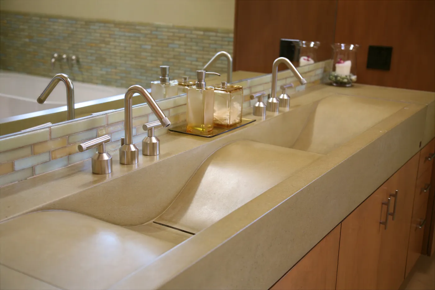 The concrete trough basins with brushed steel faucets and a glass mosaic band