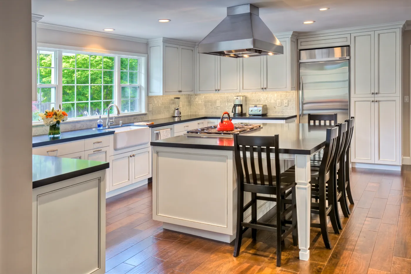 The kitchen seen wide, the island cooktop and stainless hood set against white cabinetry