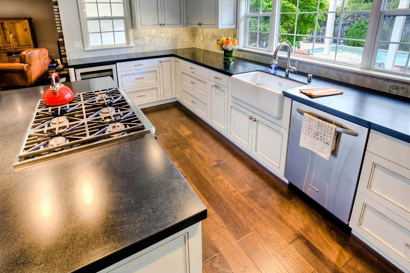 Farmhouse sink below the window with honed black counters, the island cooktop in the foreground