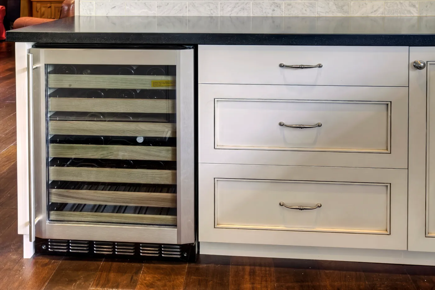 Undercounter wine refrigerator standing open beside a bank of drawers