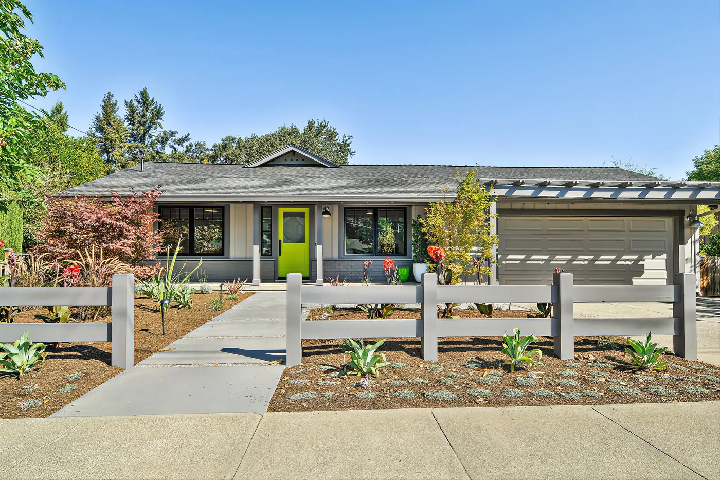 The remodelled house from the street, a chartreuse front door under the porch and a pergola over the garage