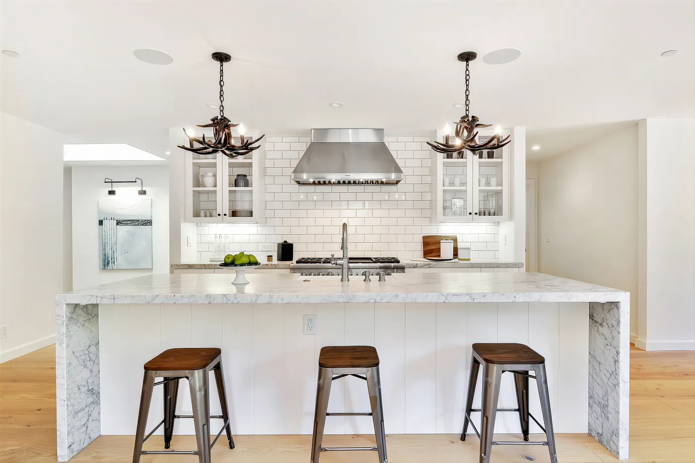 Marble island with counter stools below a pair of antler chandeliers