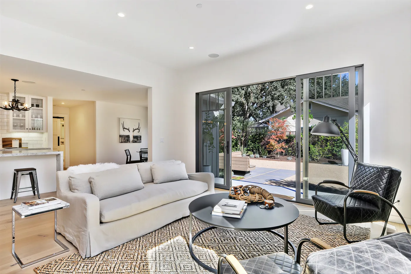 Living room with sliding doors folded open to the patio, the kitchen beyond