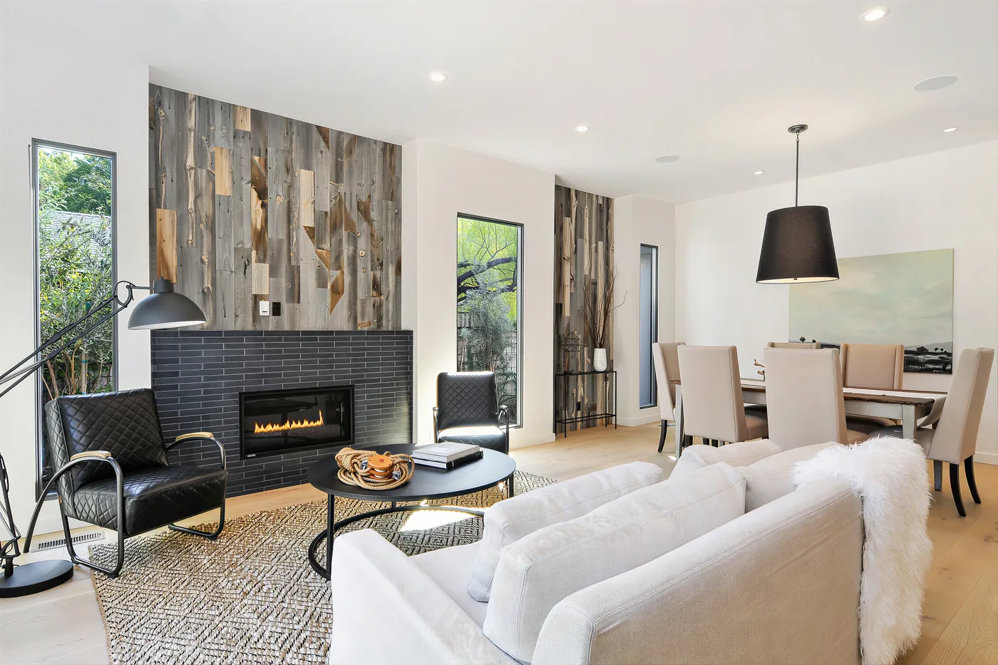 Black tiled fireplace set into the reclaimed timber wall, the dining table beyond