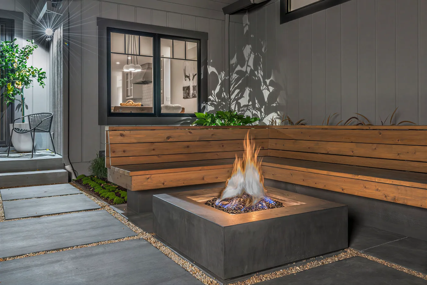 The fire table alight beside the bench, the kitchen window lit behind