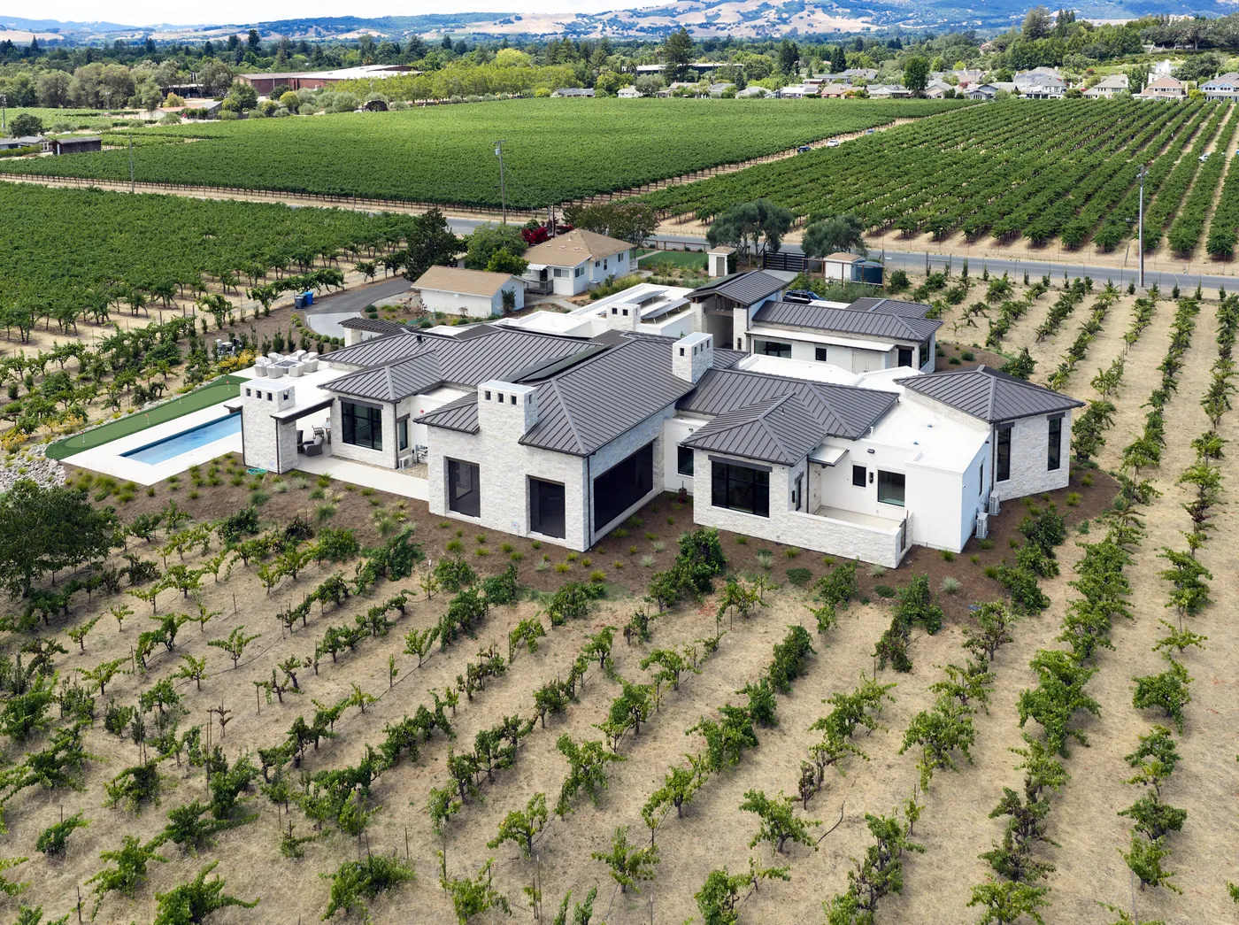 Aerial view of the house and pool set among the vineyard rows, the valley beyond