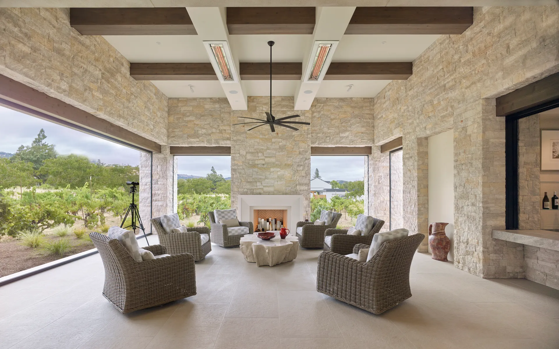 Covered loggia with a stone fireplace and overhead heaters, open to the vineyard