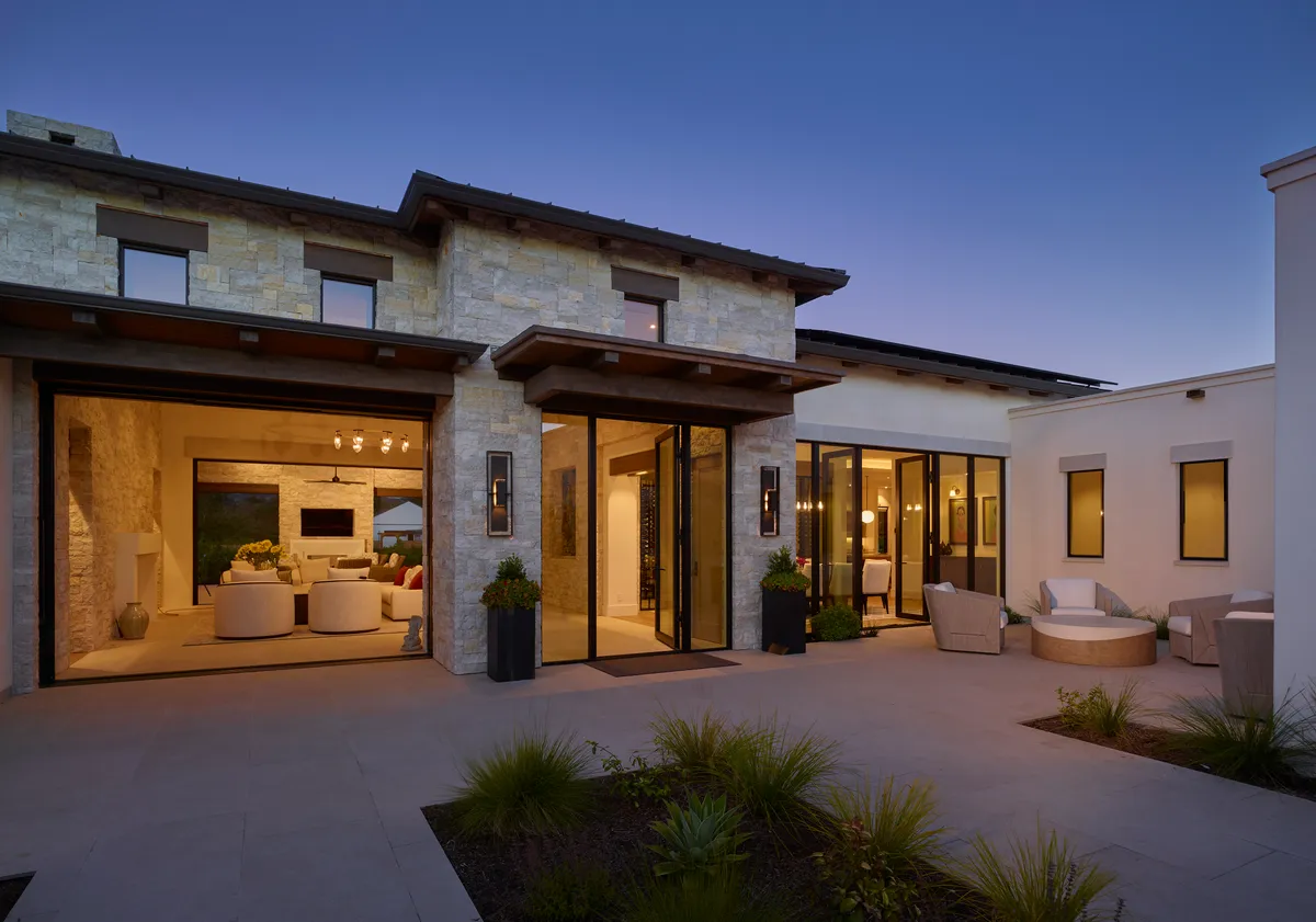 The house at dusk from the terrace, glass doors folded open to the lit living room