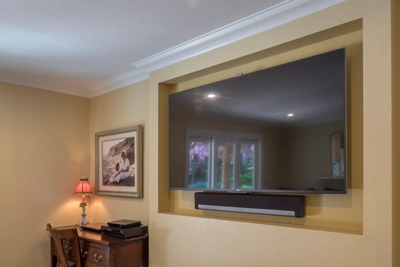 Television recessed flush into the wall above a soundbar shelf