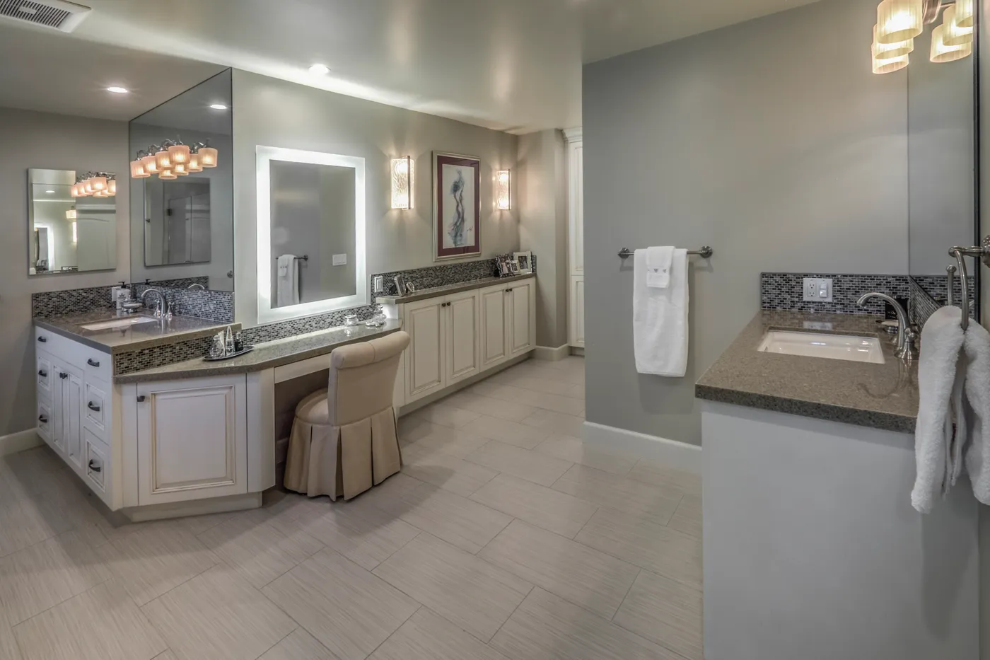 Vanity run with a lit mirror and a seated make-up station between the basins