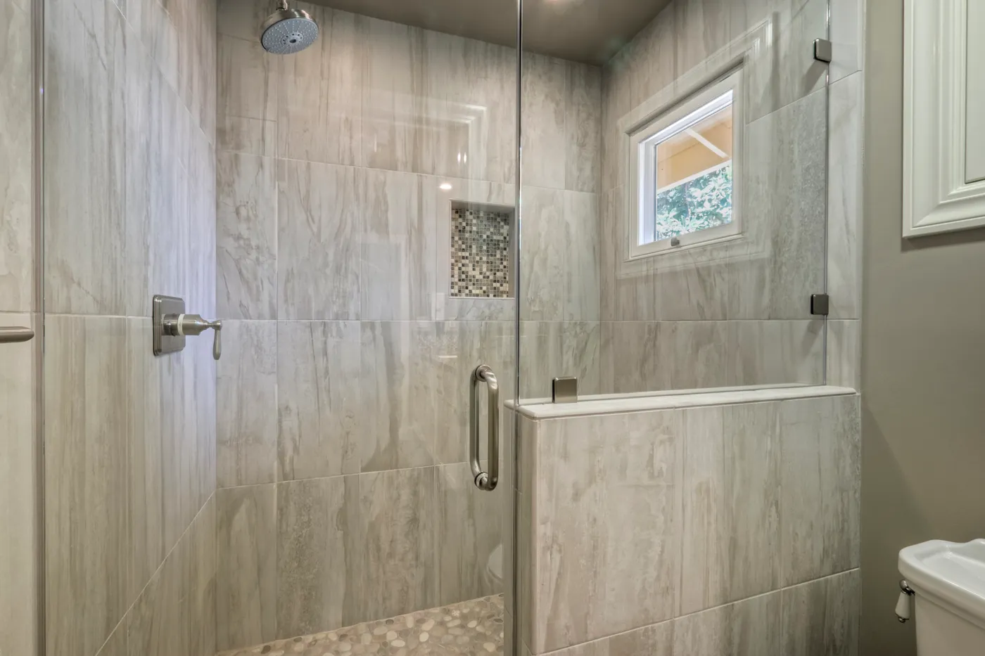 Walk-in shower in travertine with a glass door and a tiled niche