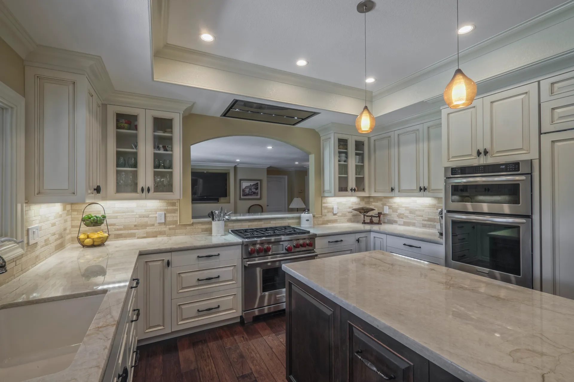 Kitchen with cream cabinetry, a stainless range below a flush ceiling hood and wall ovens alongside